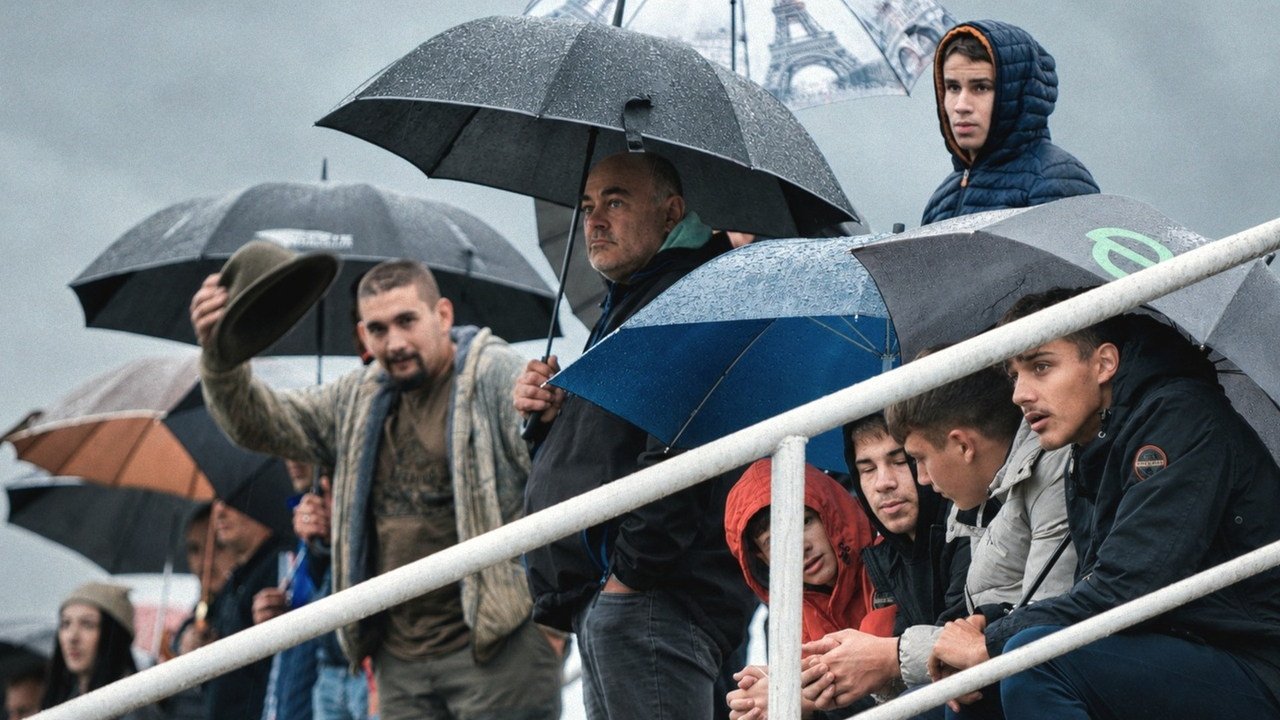 Spectators sheltering under umbrellas at a local football match near Petrova Gora